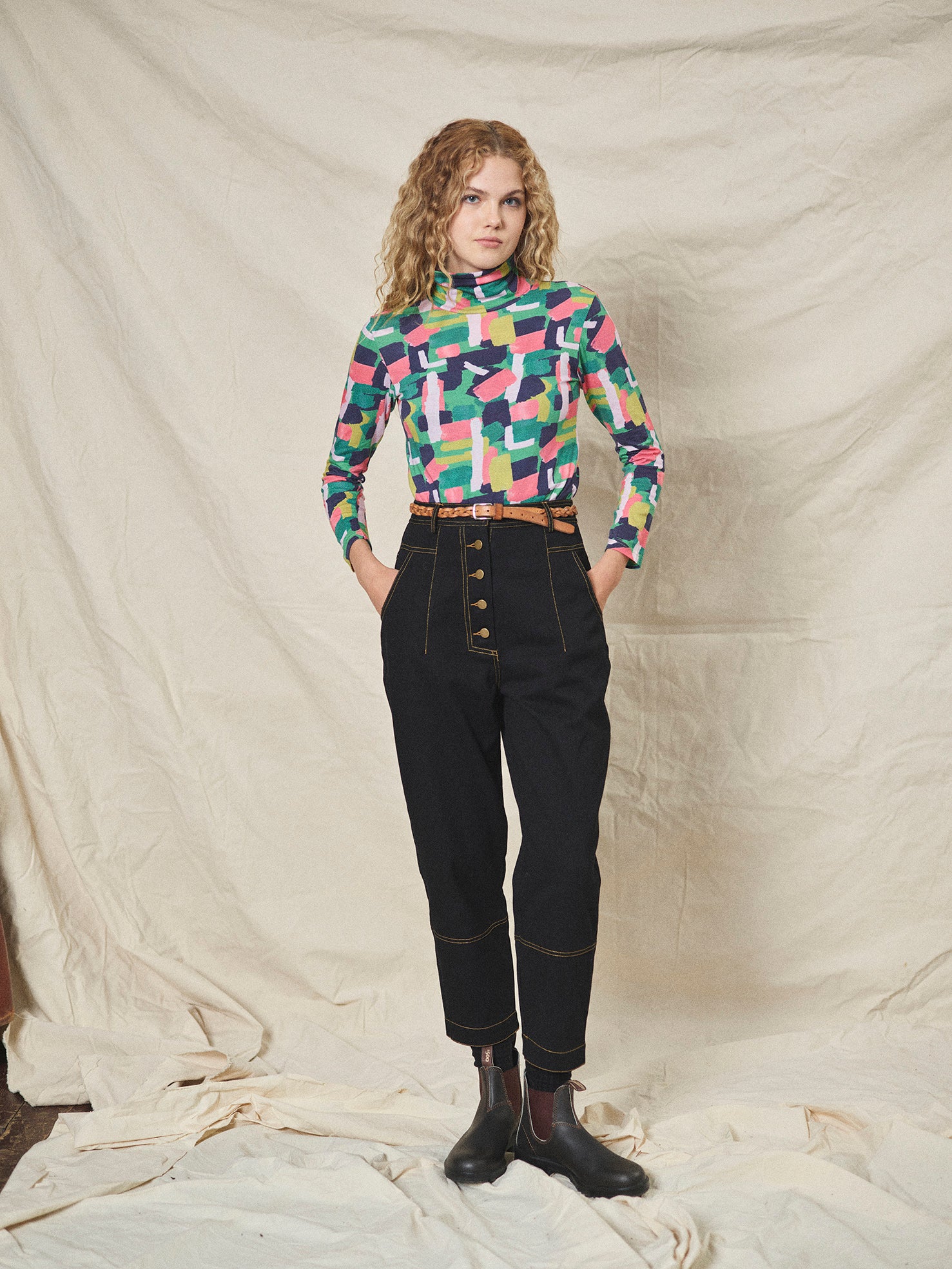 A pair of black cotton drill trousers with a high waist, wide beltband, and 5 button fly front. Features include slanted side pockets and raw stitching.