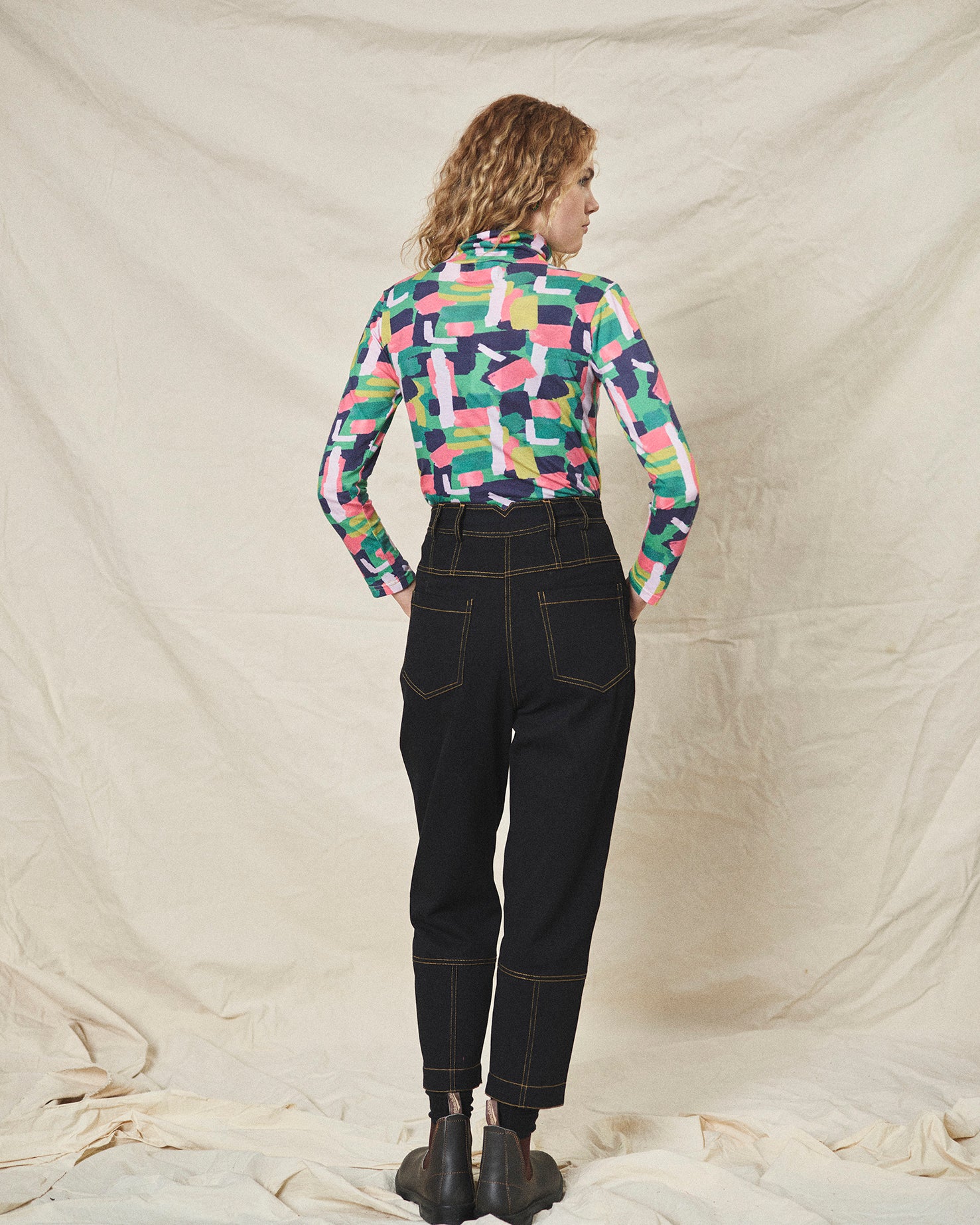 A pair of black cotton drill trousers with a high waist, wide beltband, and 5 button fly front. Features include slanted side pockets and raw stitching.