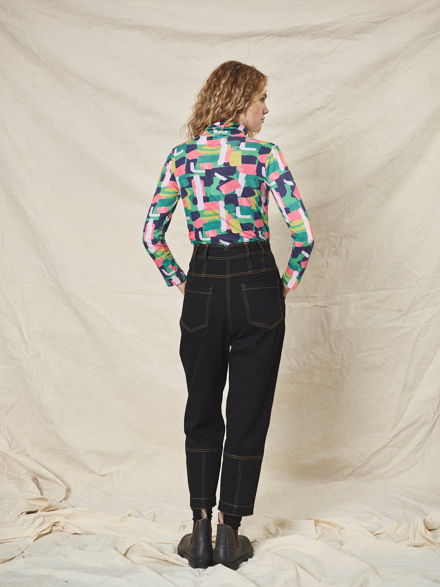 A pair of black cotton drill trousers with a high waist, wide beltband, and 5 button fly front. Features include slanted side pockets and raw stitching.