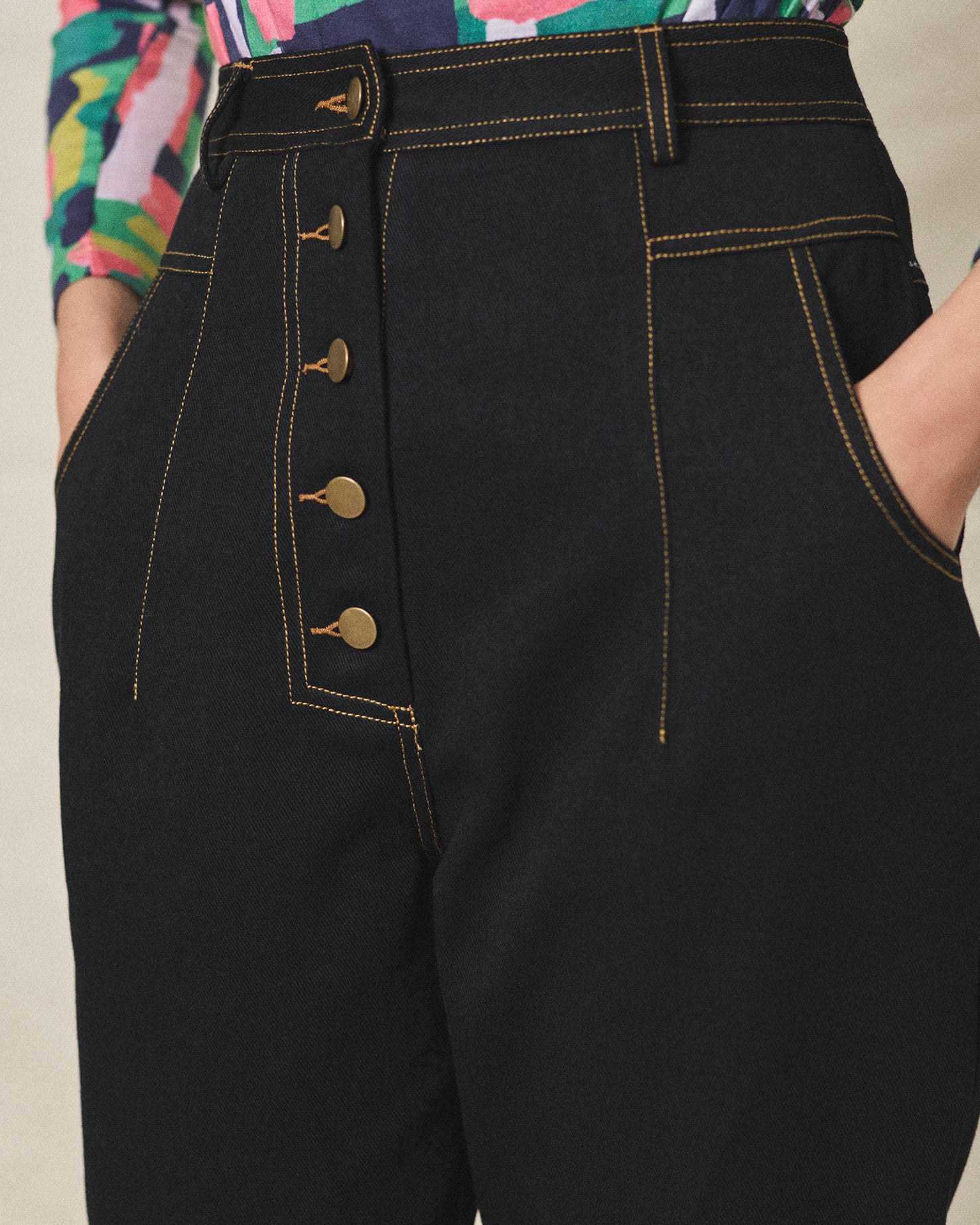 A pair of black cotton drill trousers with a high waist, wide beltband, and 5 button fly front. Features include slanted side pockets and raw stitching.