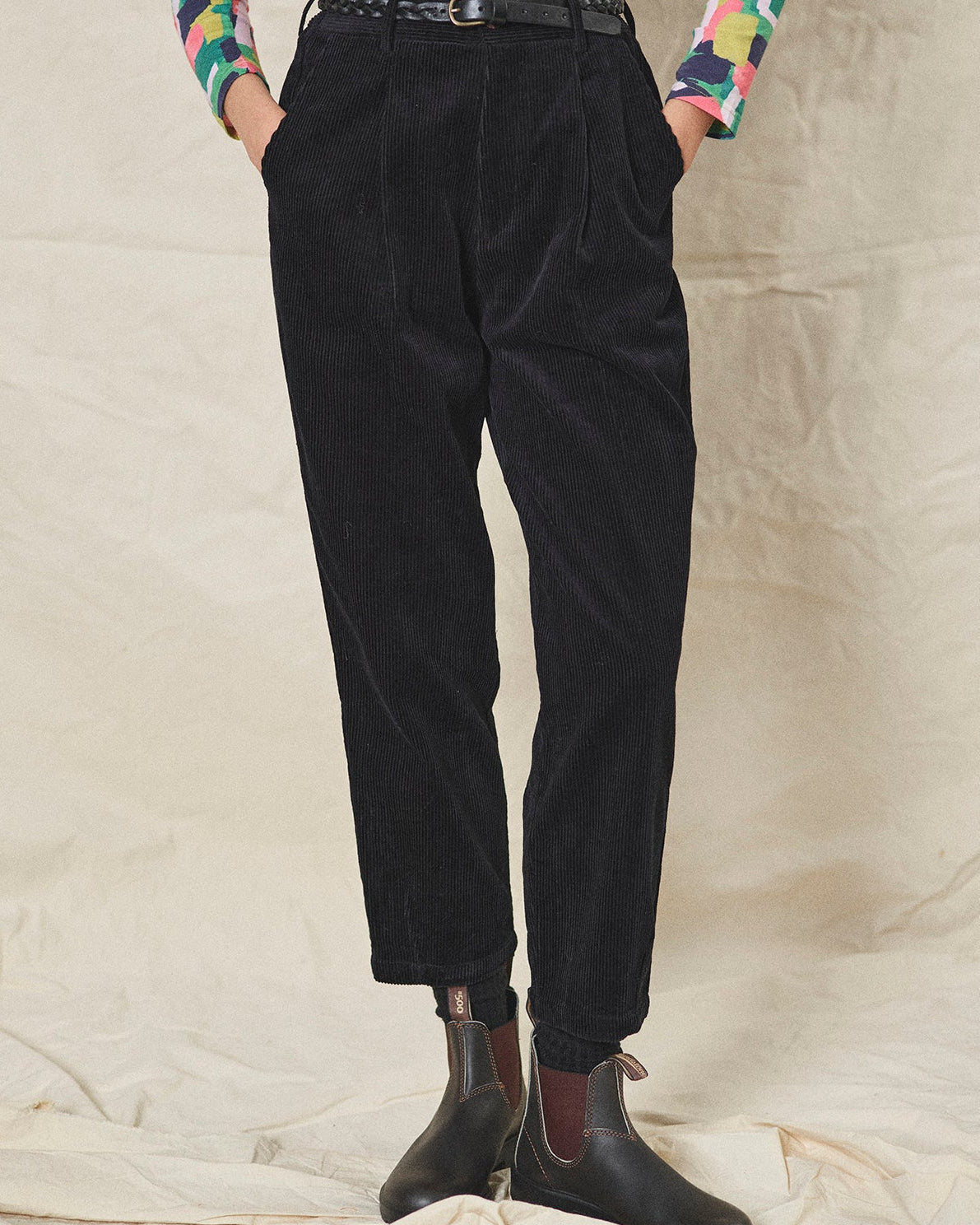 Person wearing black corduroy pants and colourful shirt on a neutral background