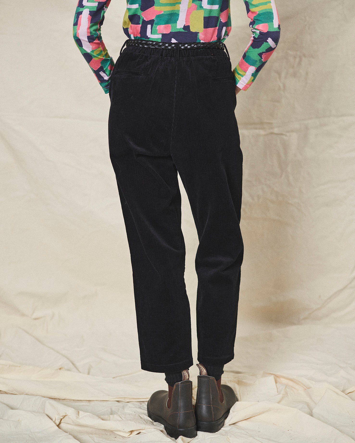 Person wearing black corduroy pants and colourful shirt on a neutral background