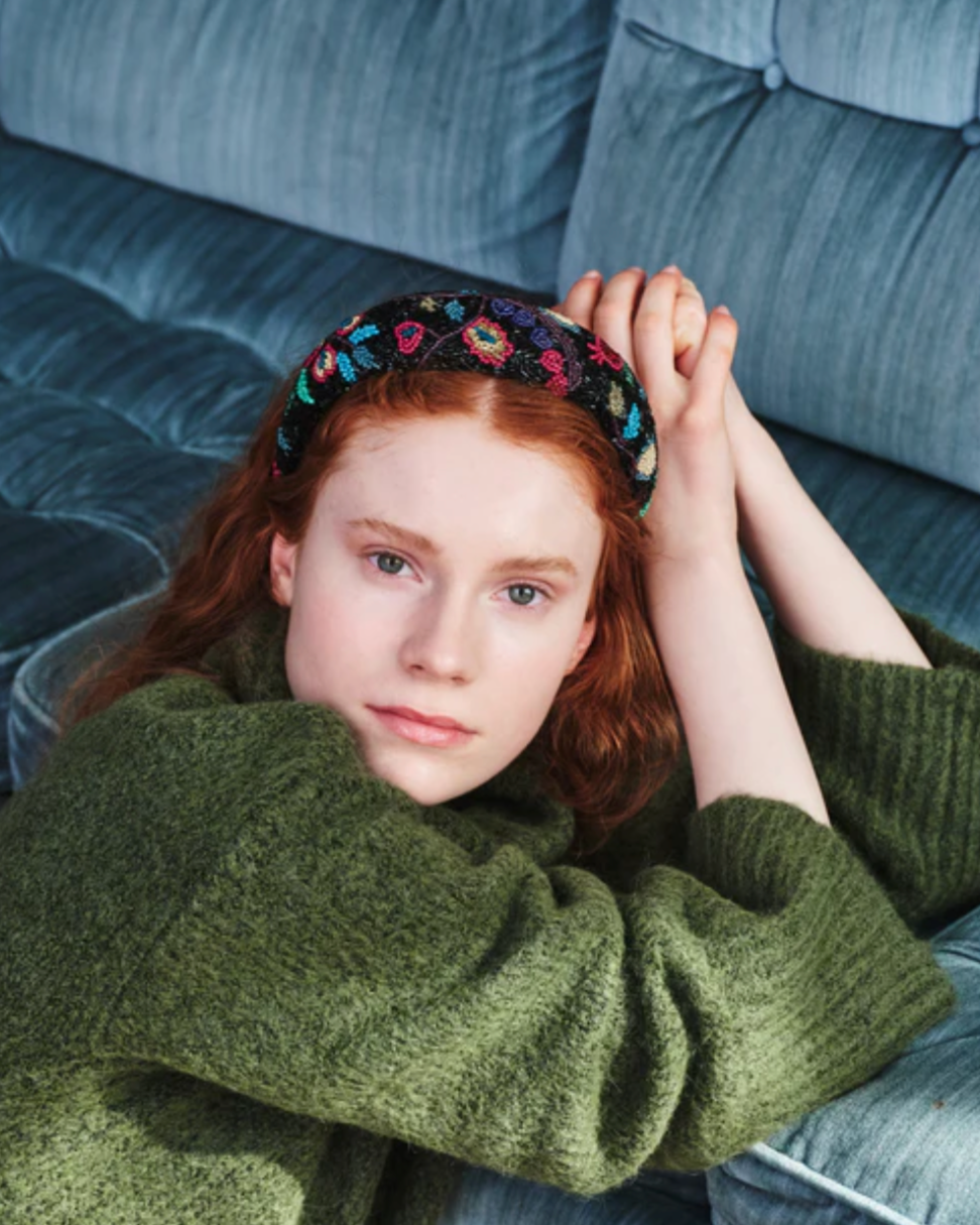 Person wearing a green sweater and floral headband sitting on a blue couch.