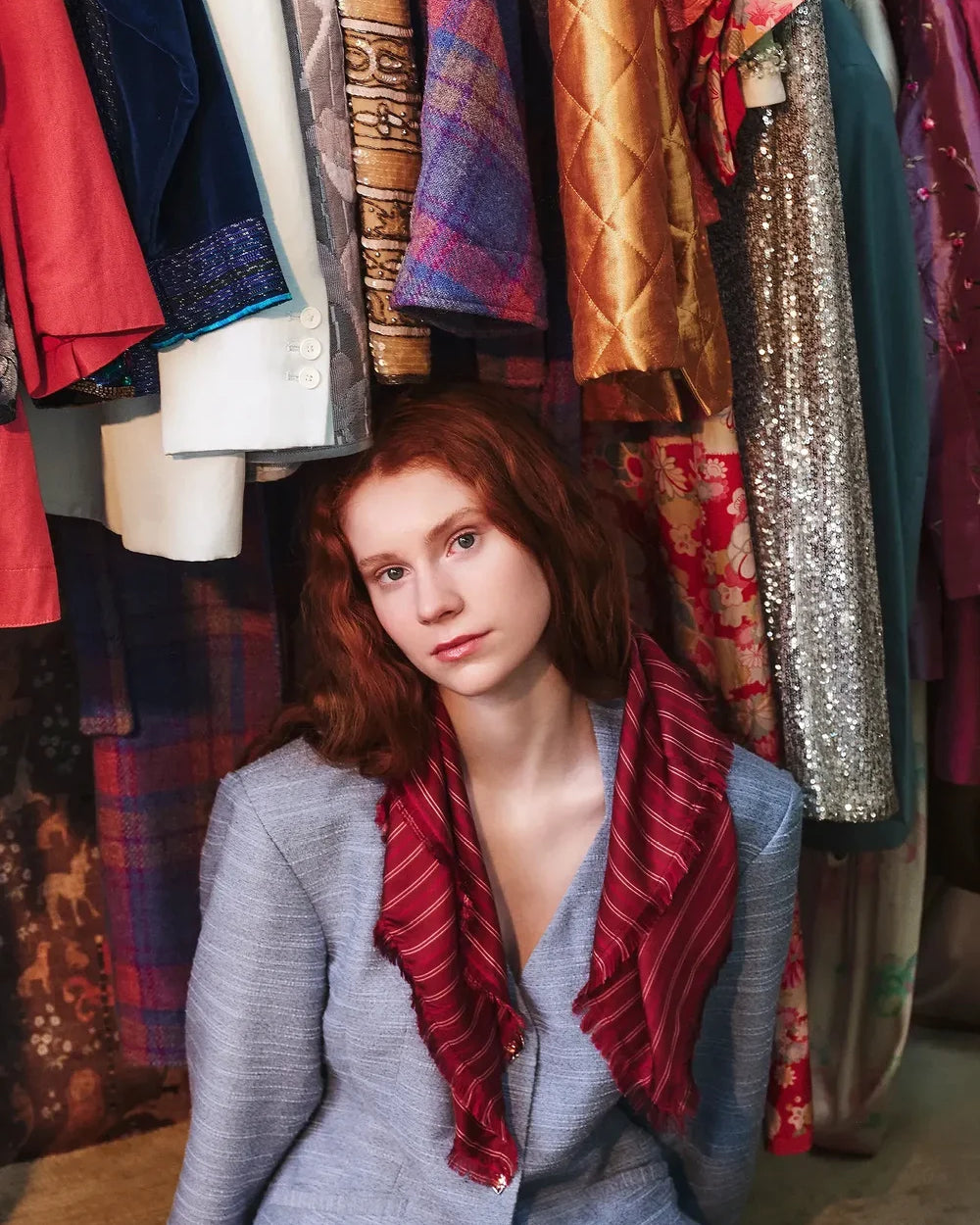 Woman with red hair sitting in front of a rack of colorful clothing