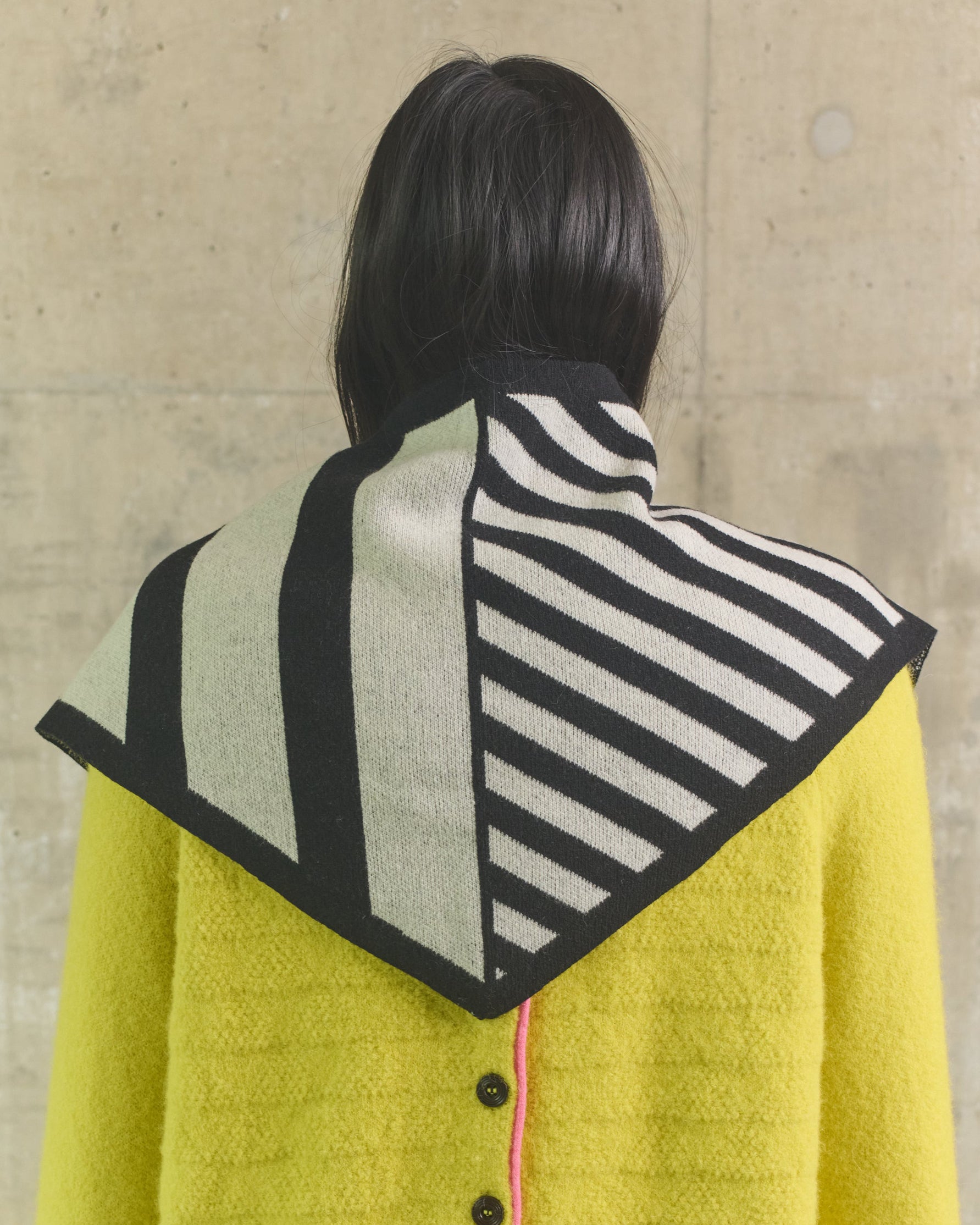 Person wearing a yellow coat with a patterned hood against a beige wall