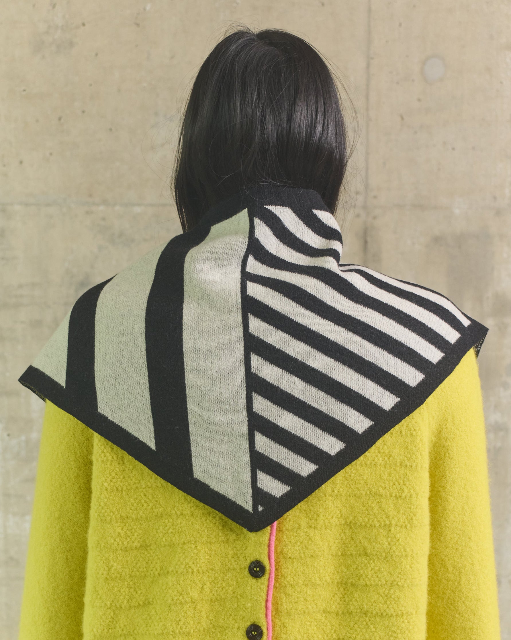 Person wearing a yellow coat with a patterned hood against a beige wall