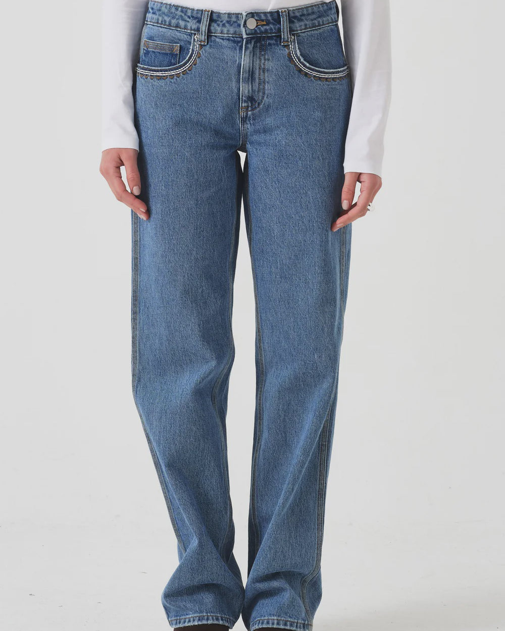 Person wearing blue jeans and a white shirt on a plain background