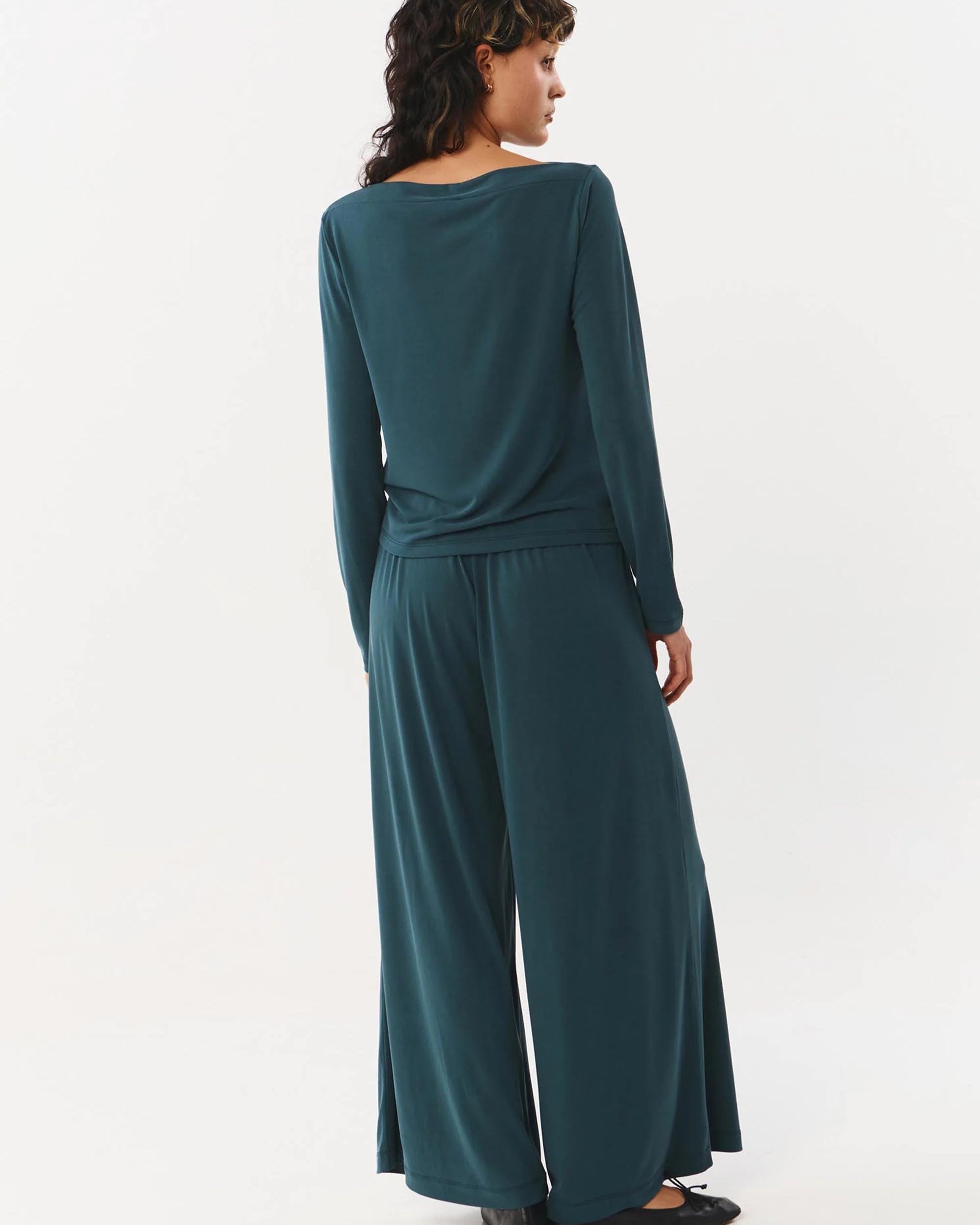 Woman wearing a teal long-sleeve jumpsuit on a white background