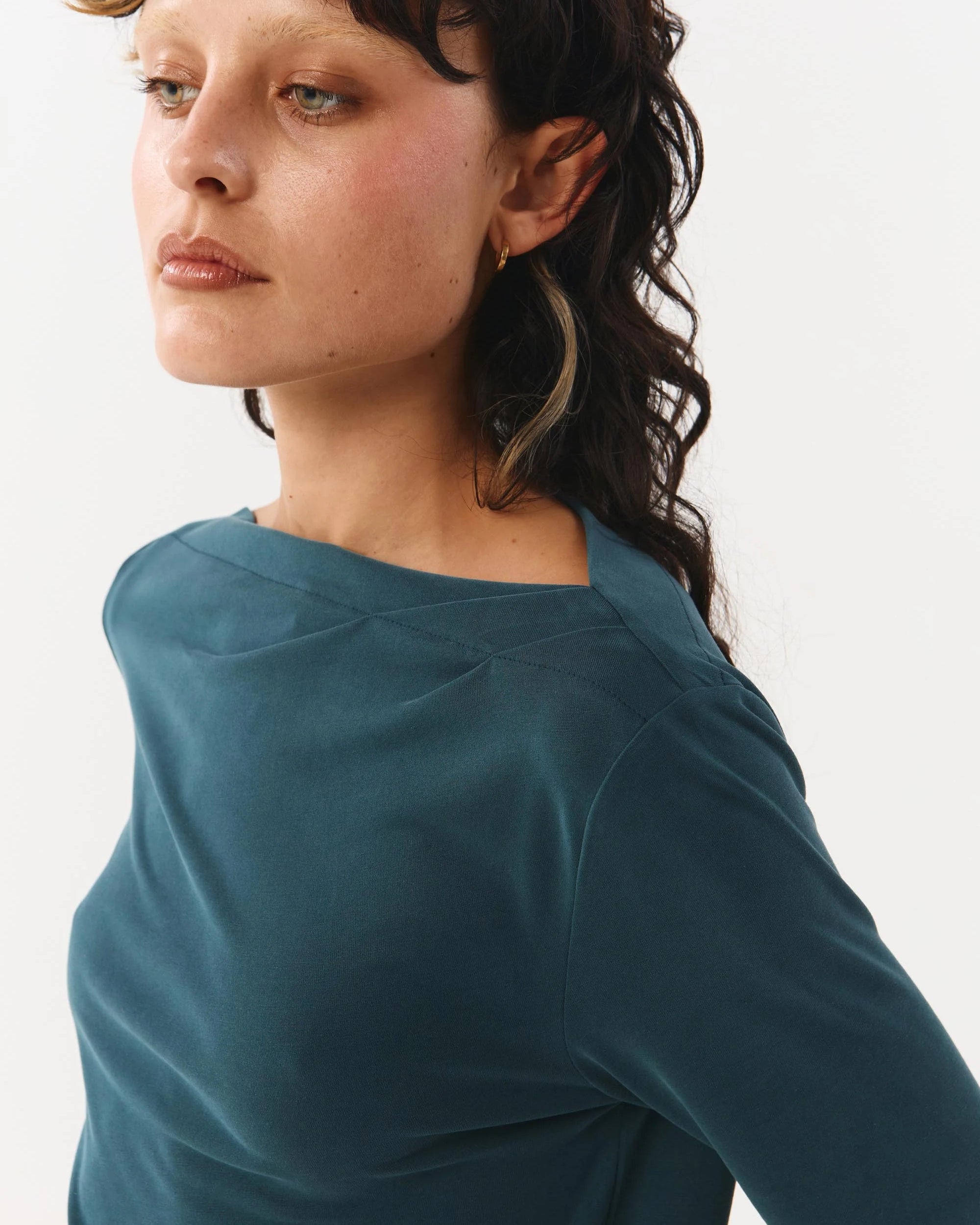 Woman wearing a teal long-sleeve top against a white background