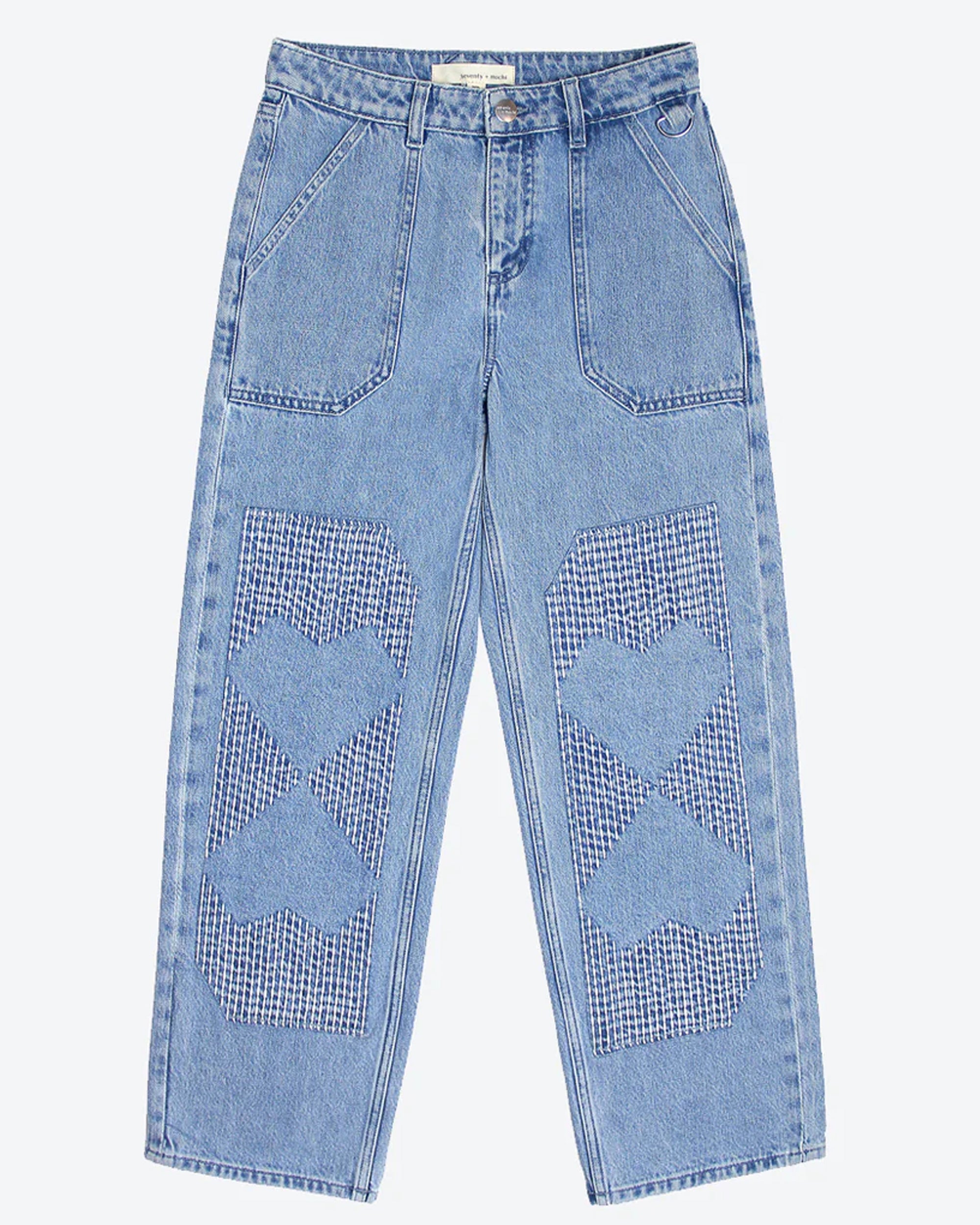 A pair of blue carpenter style jeans with embroidery on the front legs and a center front seam, displayed against a white background.