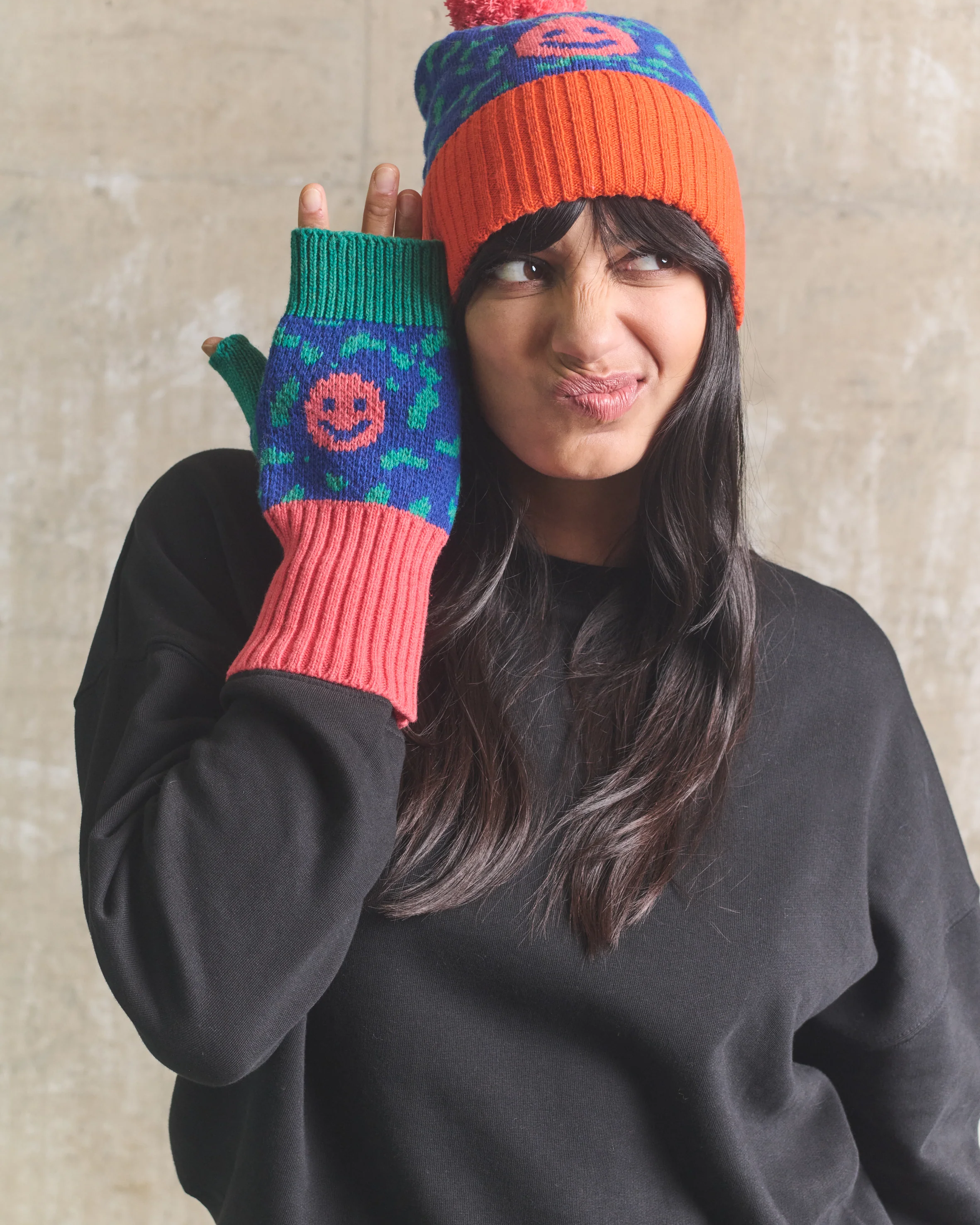Person wearing colorful knit hat and gloves against a textured wall.