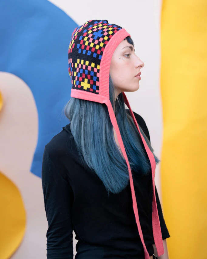 Person wearing a colorful patterned hat with long ear flaps against a multicolored background
