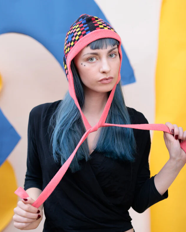 Person wearing a colorful knit hat with a pink strap against a multicolored background
