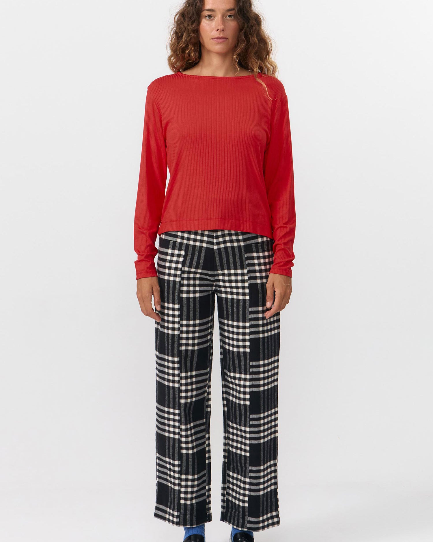 Person wearing a red long-sleeve top and plaid pants on a white background