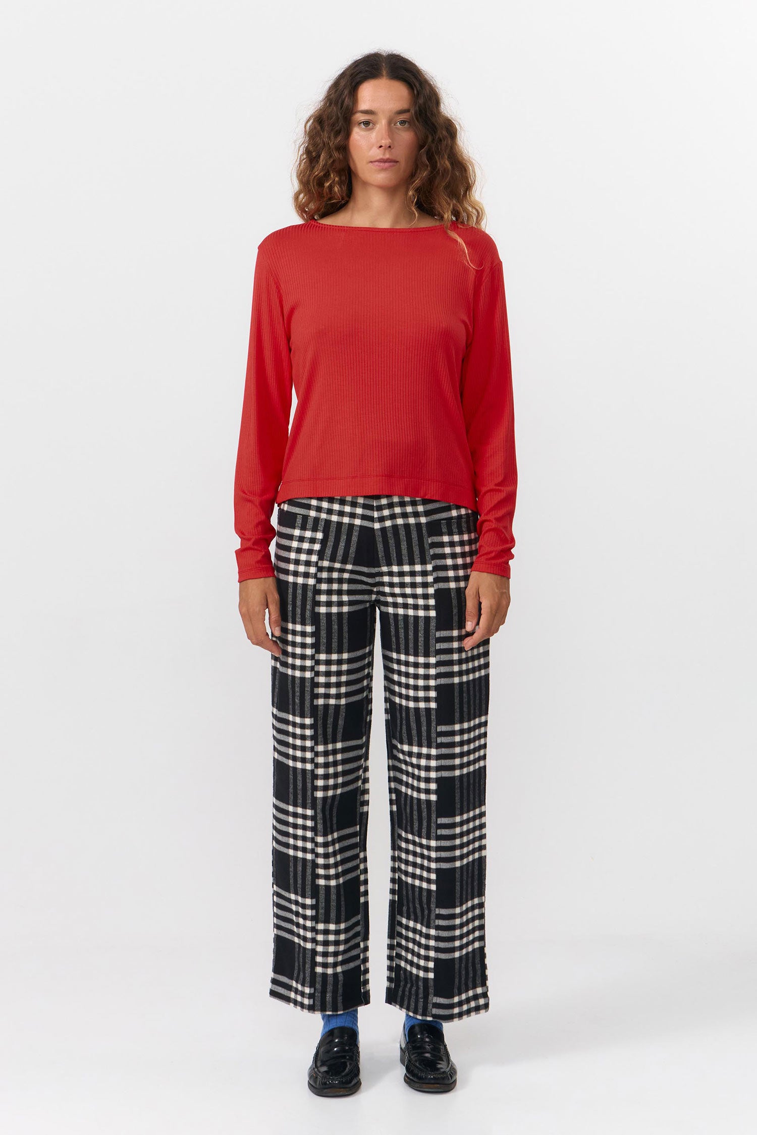 Person wearing a red long-sleeve top and plaid pants on a white background