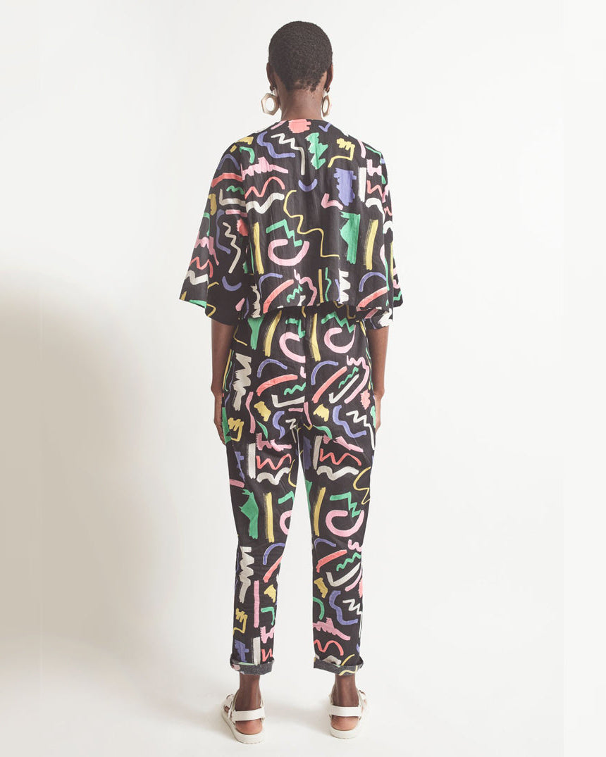 A pair of black holiday trousers with a multicolored scribble print, featuring a high waist, tapered leg, and side pockets.