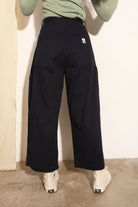 Person wearing black pants with a visible brand logo against a plain background