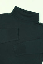Close-up of a dark green turtleneck sweater with patch details on a light background