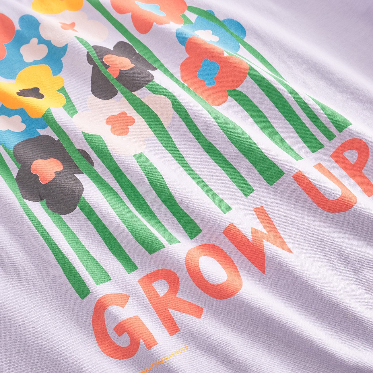 A relaxed fit purple T-shirt with a graphic of flowers and the text 'GROW UP' designed by Luke John Arnold.
