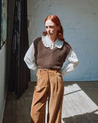 Woman wearing a brown vest, white shirt, and tan pants standing indoors.