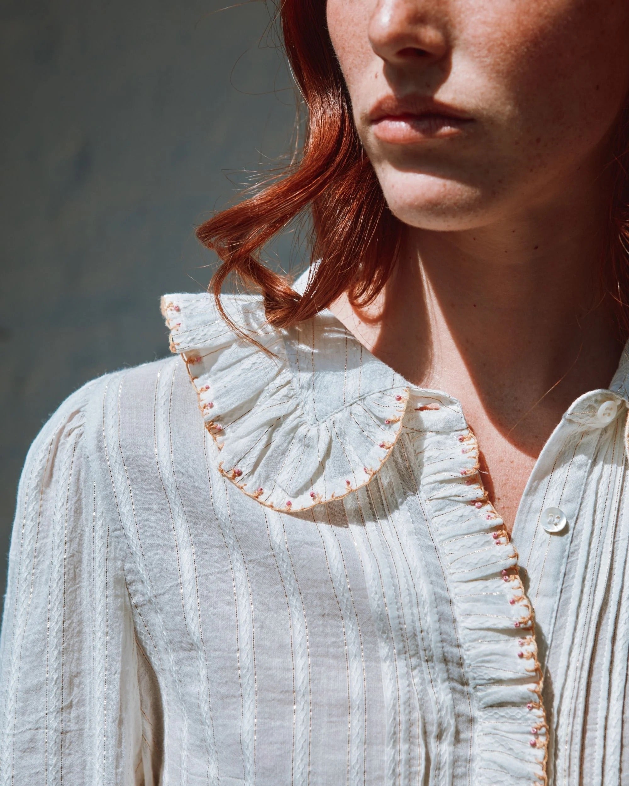 Close-up of a person wearing a light-colored blouse with a ruffled collar against a neutral background