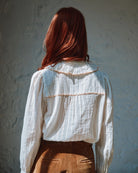 Person wearing a white blouse with brown accents against a textured wall.