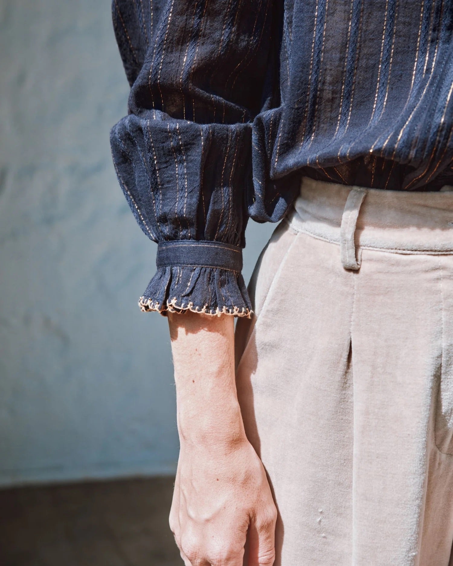 Close-up of a person wearing a blue striped shirt with ruffled cuffs against a neutral background