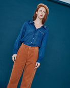 Woman wearing a blue shirt and brown pants against a blue background