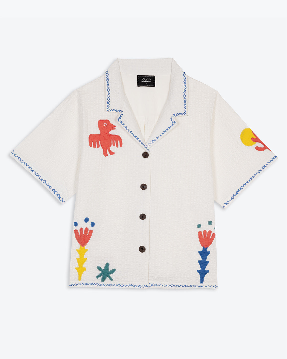 A white cotton blouse with colorful hand embroidery details, featuring a notched collar, wide cut sleeves, and a boxy fit.