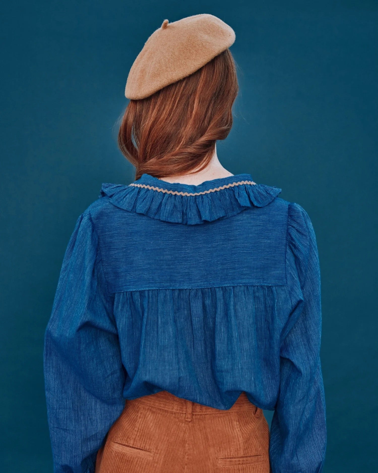 Person wearing a blue blouse and brown beret against a dark blue background