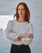 Woman wearing a polka dot blouse against a textured white wall