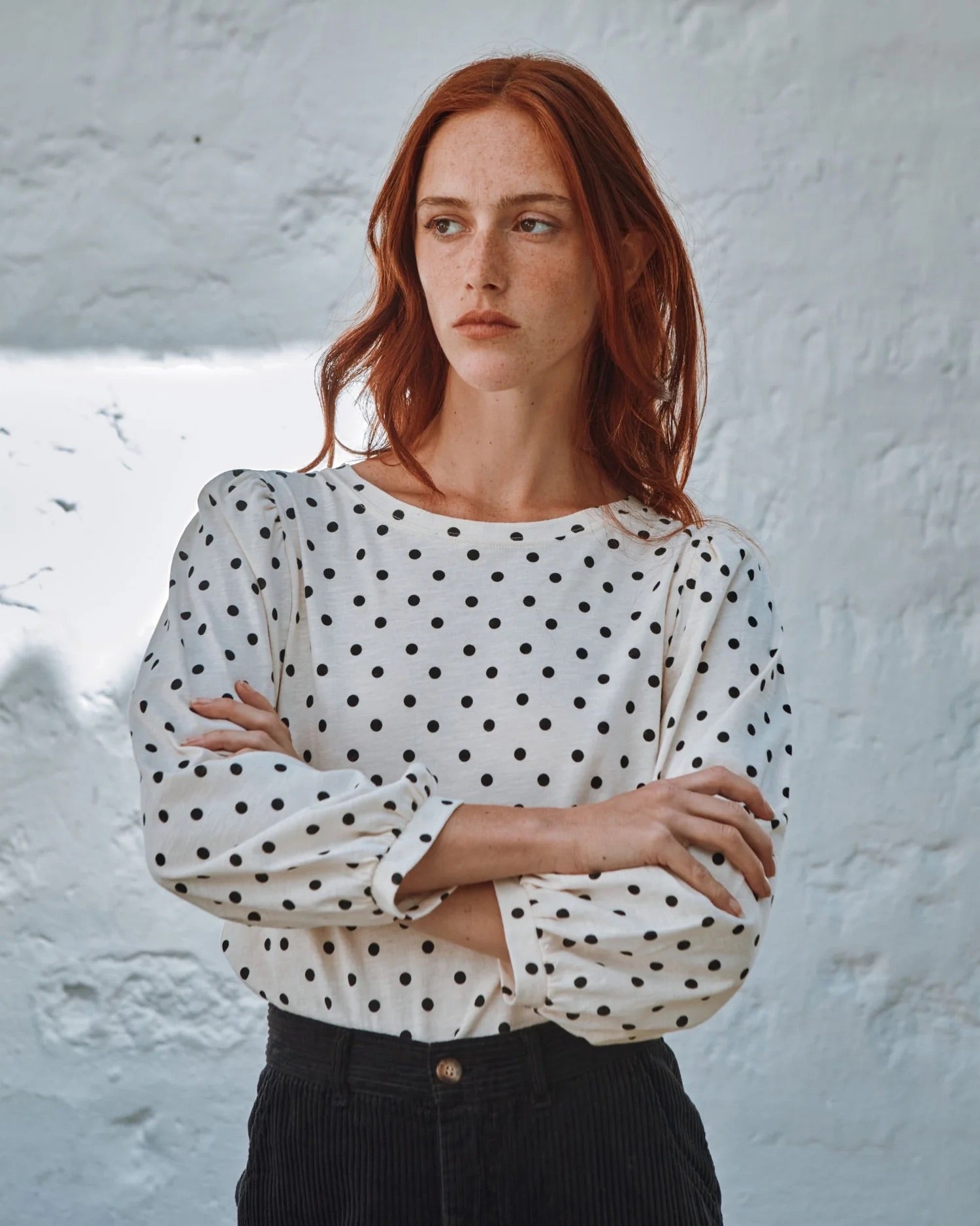 Woman wearing a polka dot blouse against a textured white wall