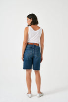 Woman wearing a white sleeveless top and blue denim shorts on a white background