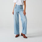 A pair of high-waisted, wide leg jeans with a button-up front in an oceanic blue wash. The jeans are worn with brown ankle boots.