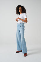 A pair of high-waisted, wide leg jeans with a button-up front in an oceanic blue wash. The jeans are worn with brown ankle boots.