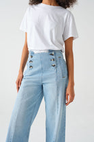A pair of high-waisted, wide leg jeans with a button-up front in an oceanic blue wash. The jeans are worn with brown ankle boots.