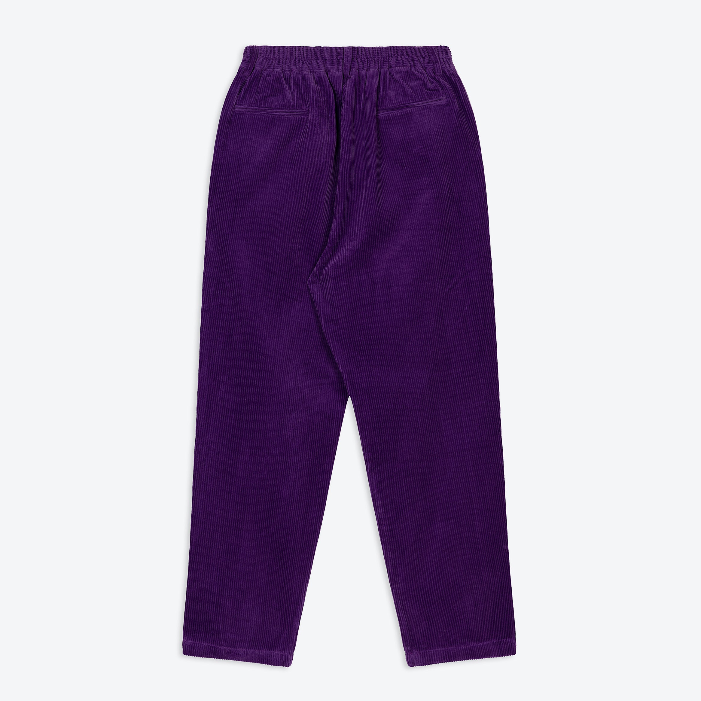 Person wearing purple corduroy pants with a checkered shirt and black boots on a textured beige background