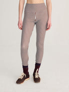A model from the waist down wearing high-waisted leggings with vertical brown, white, and black stripes, styled with dark maroon socks and brown sneakers against a light gray studio background.