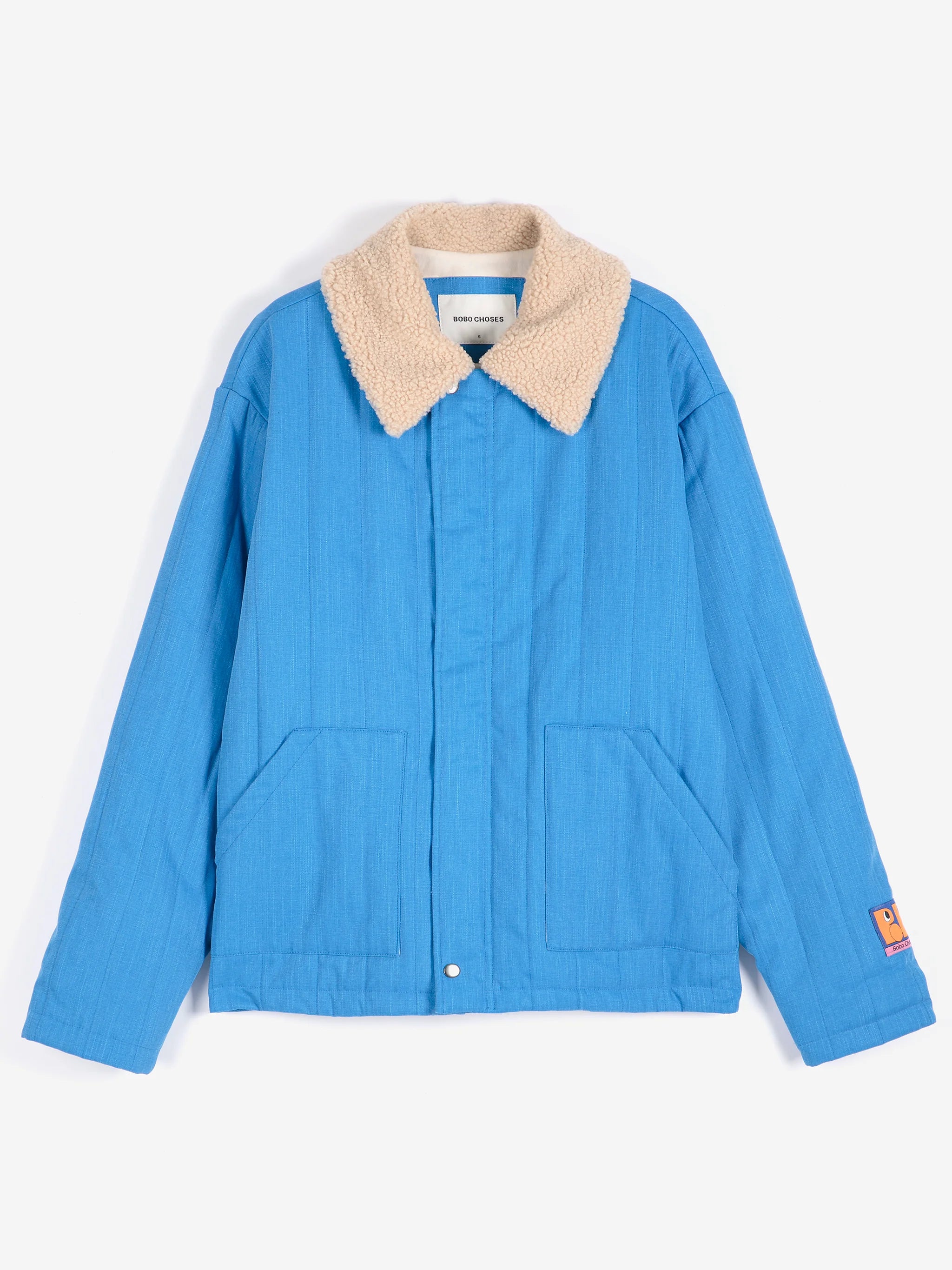 A blue quilted jacket with a beige sherpa collar, featuring front patch pockets and a small orange label on the left sleeve, displayed against a clean white background.