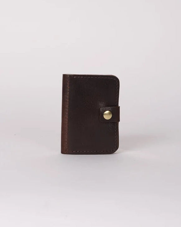 A small dark brown leather card holder or wallet with a snap button closure, standing upright on a light gray background.