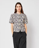 Woman wearing a patterned shirt and dark pants on a plain background