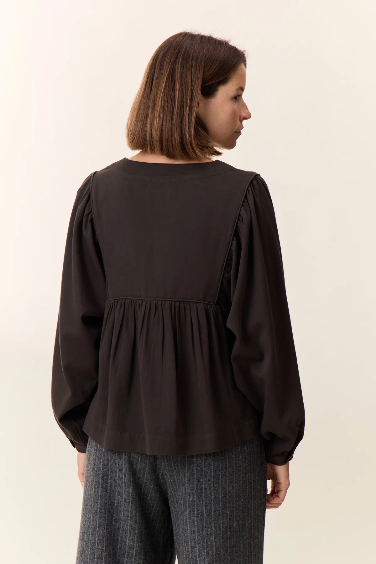 Woman wearing a dark brown blouse with long sleeves on a plain background