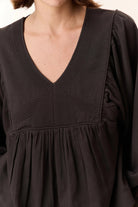 Close-up of a person wearing a black dress with a V-neckline.