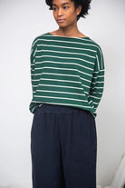 Person wearing a green and white striped sweater with navy pants against a plain background