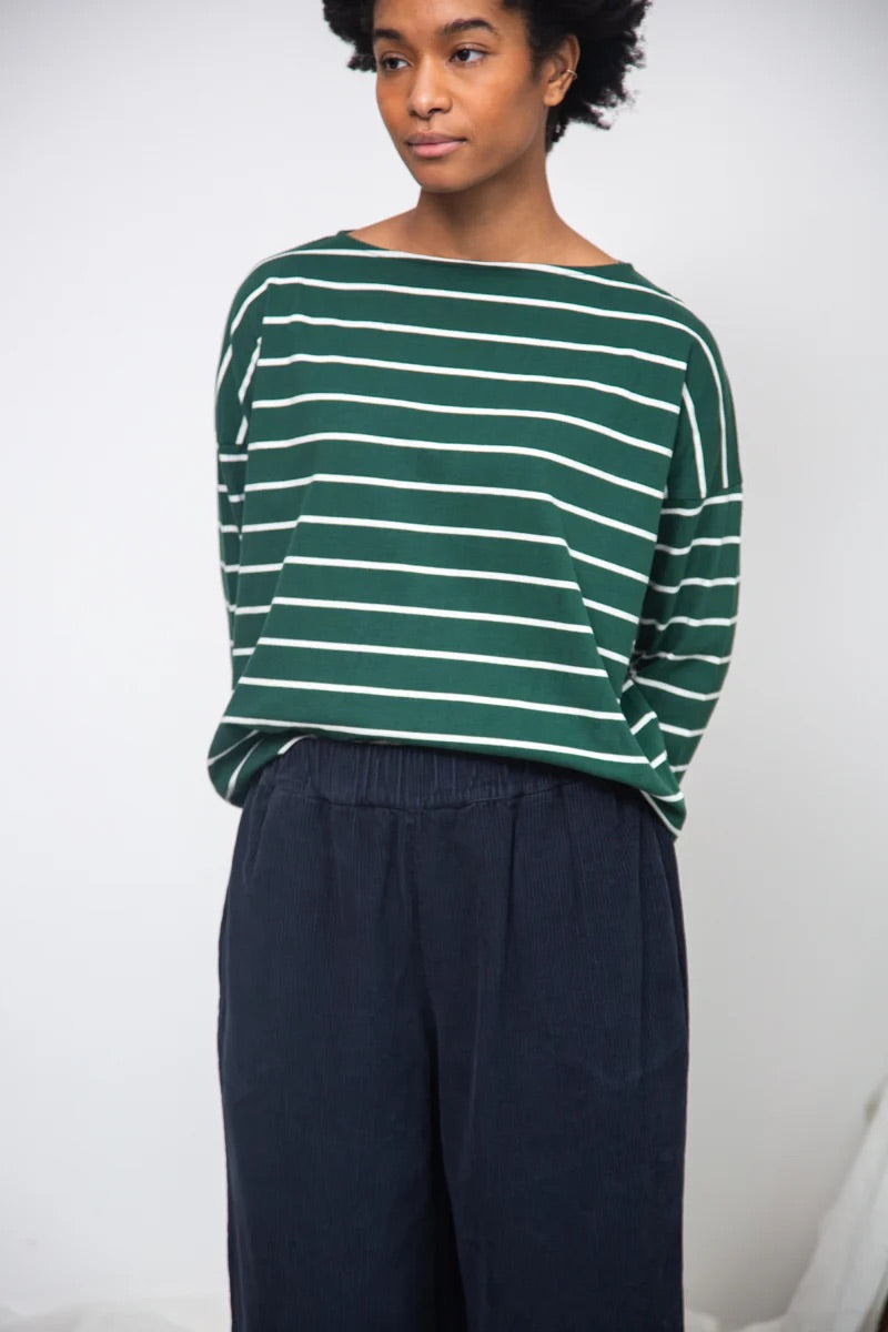 Person wearing a green and white striped sweater with navy pants against a plain background