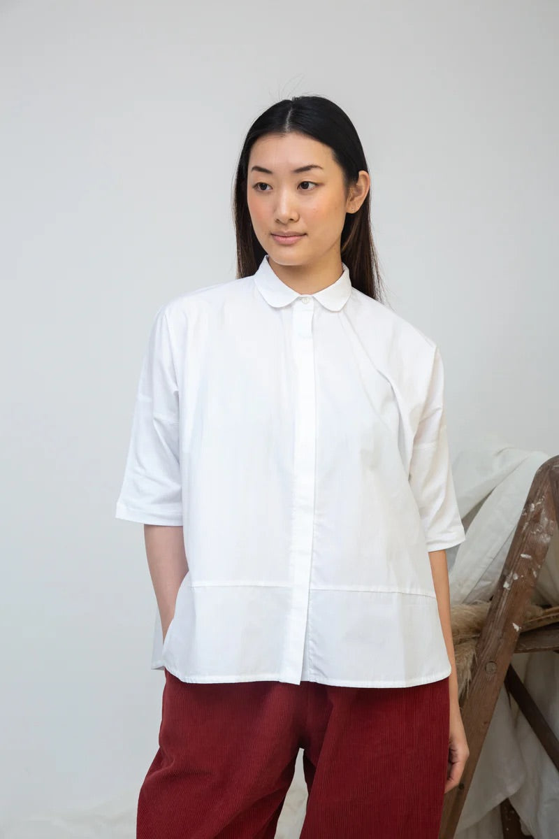 Woman wearing a white blouse and red pants against a plain background