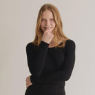 A woman wearing a black long-sleeve top with a crew neck, standing against a neutral background.