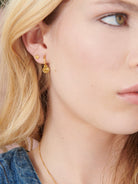 Close-up of a person wearing gold earrings with a neutral background