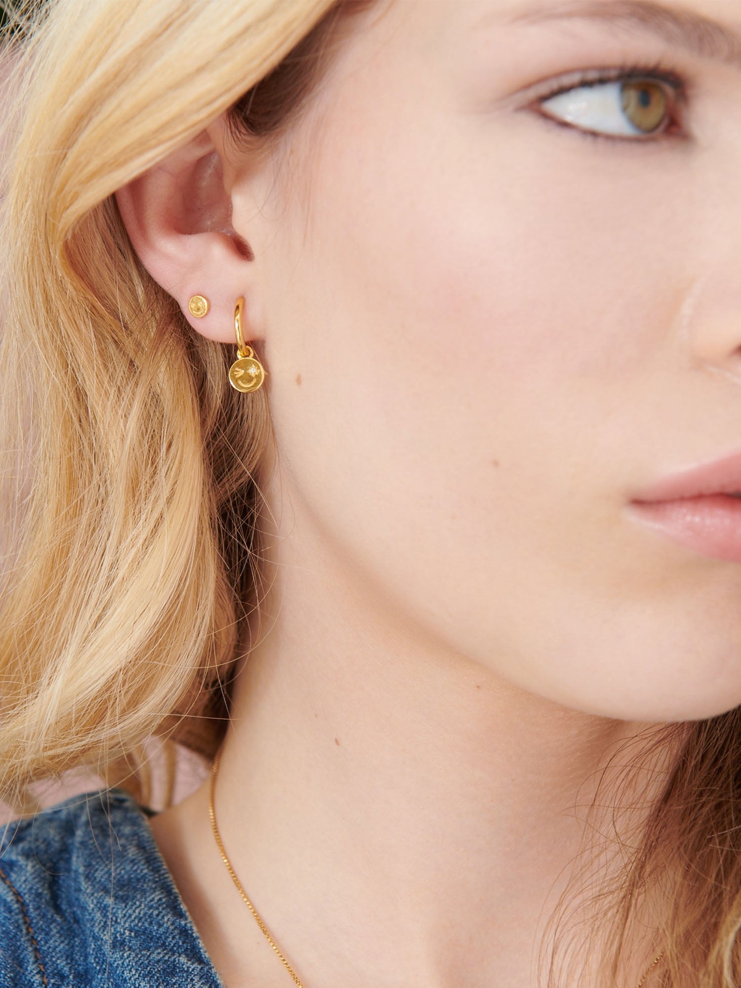 Close-up of a person wearing gold earrings with a neutral background