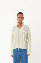 Person wearing a white blouse with ruffled details and blue jeans on a white background